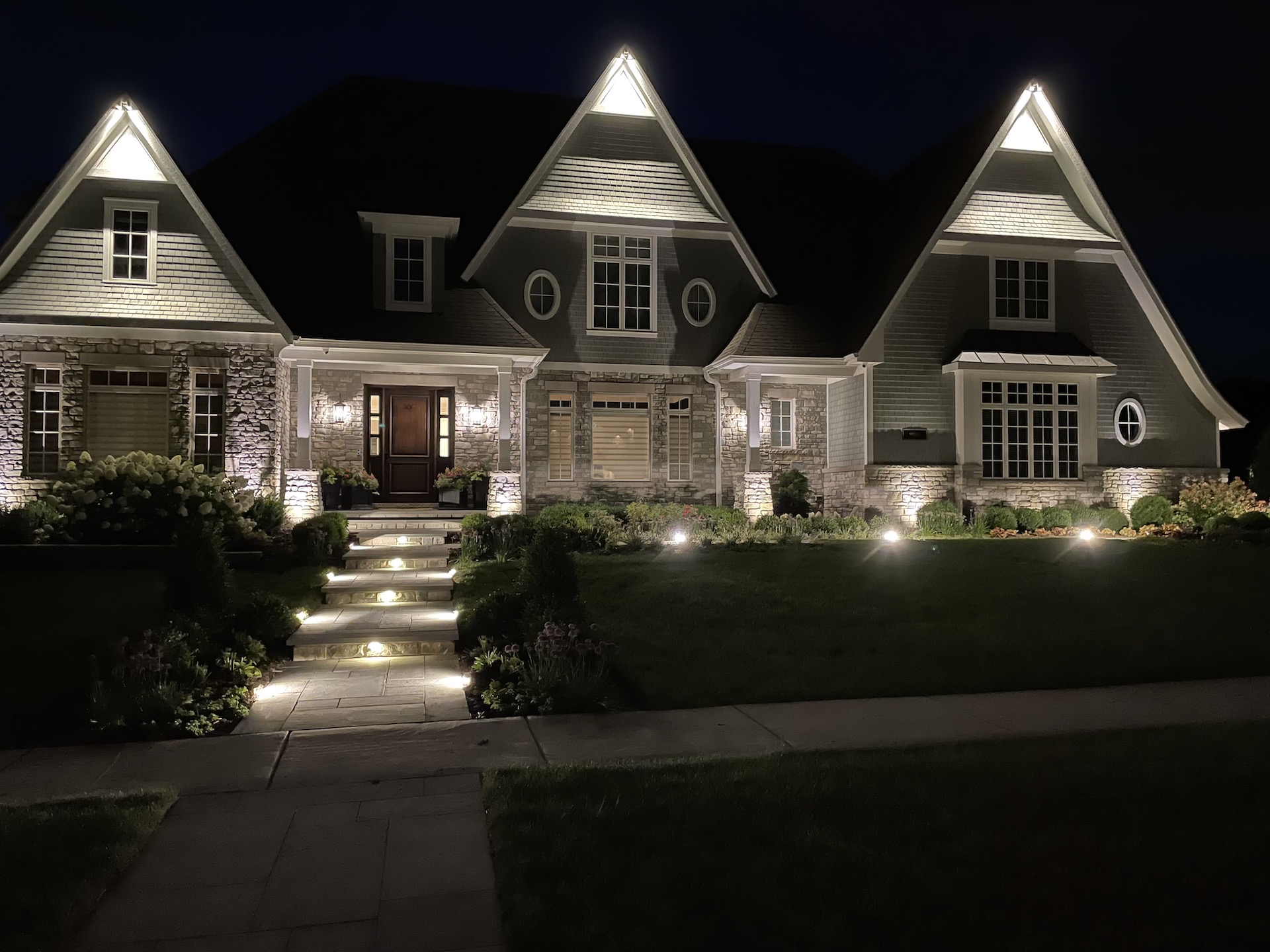 Two story gray stone house landscape lighting large front steps NEI Distributors North Reading MA.